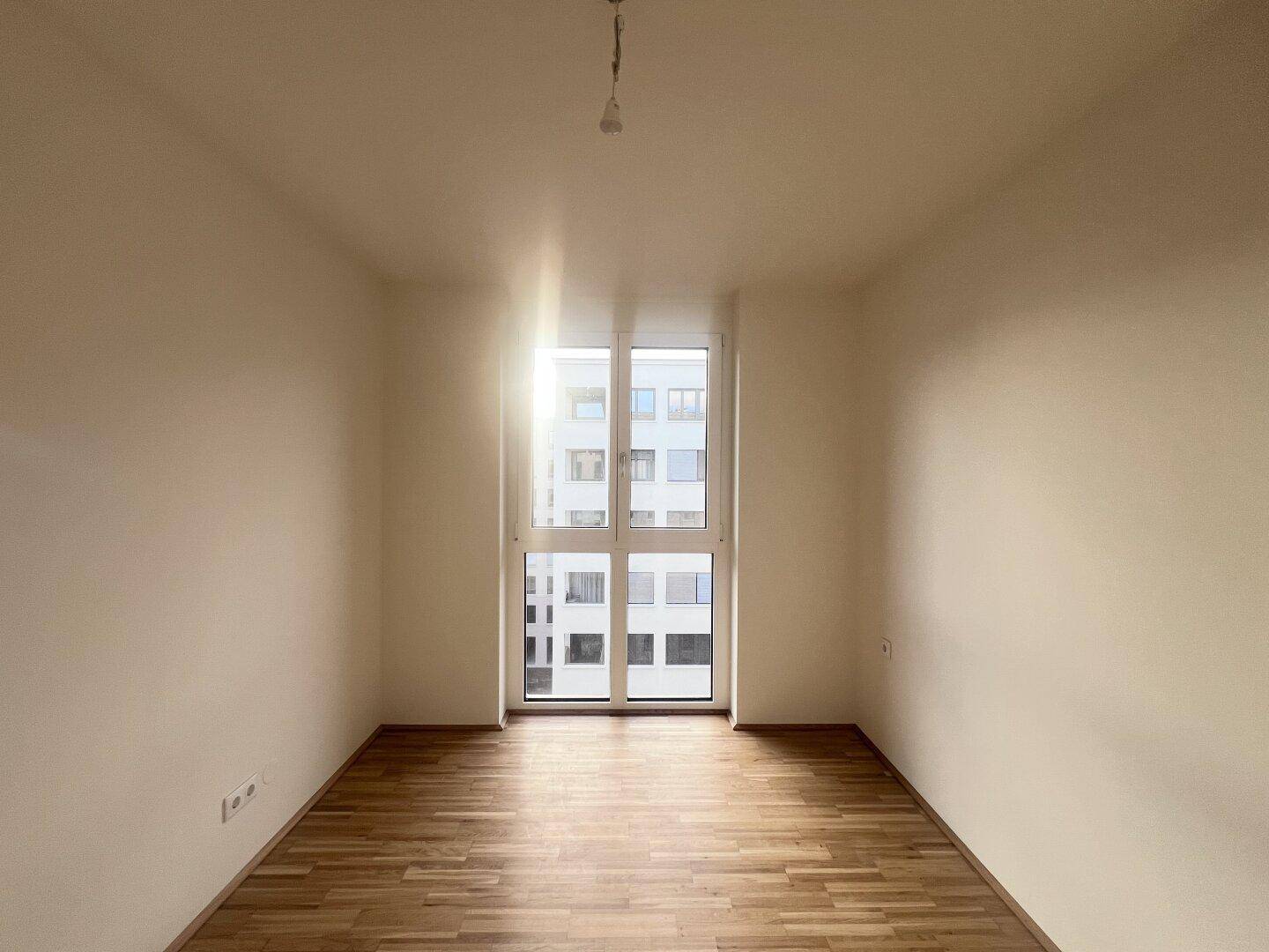 Helles Zimmer mit Parkettboden und großem Fenster, ideal als Schlaf- oder Arbeitszimmer.