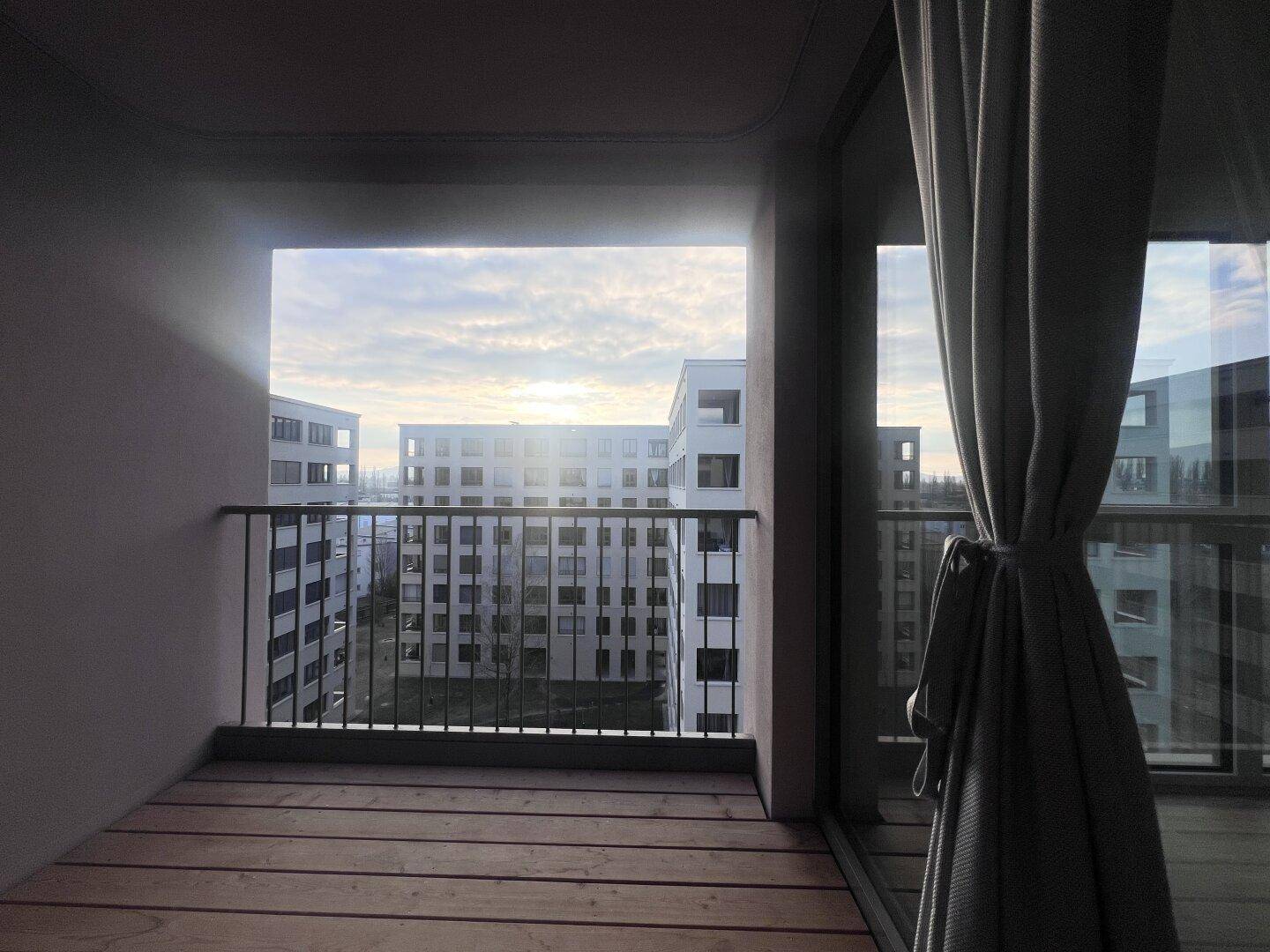 Balkon mit Holzboden und Blick auf die umliegenden modernen Gebäude.