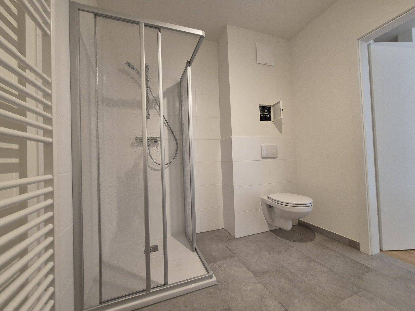 Modernes Badezimmer mit Duschkabine, wandhängendem WC und Handtuchheizkörper.