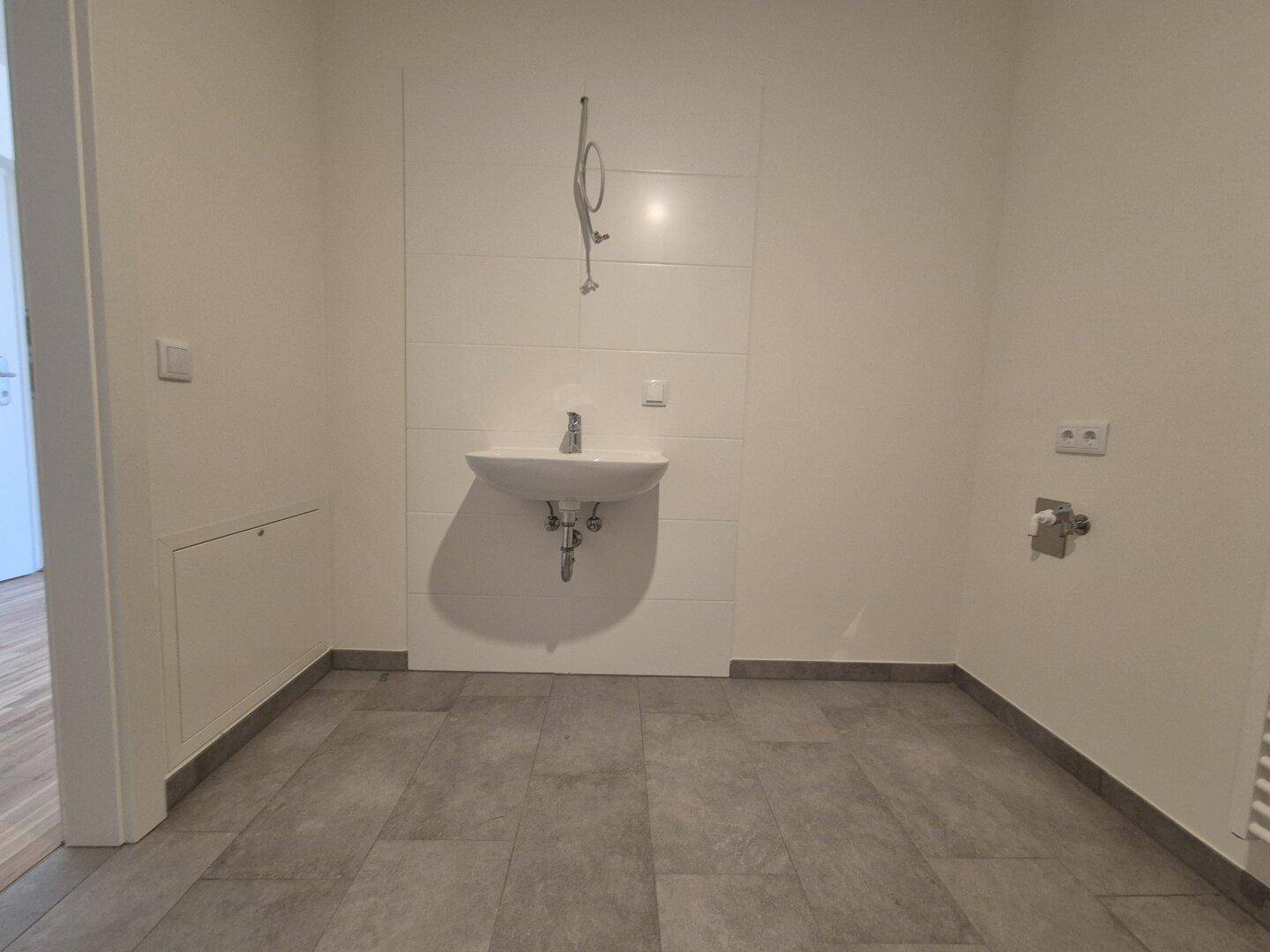 Helles Badezimmer mit Einzelwaschbecken, grauen Fliesen und vorbereiteten Duschanschlüssen.