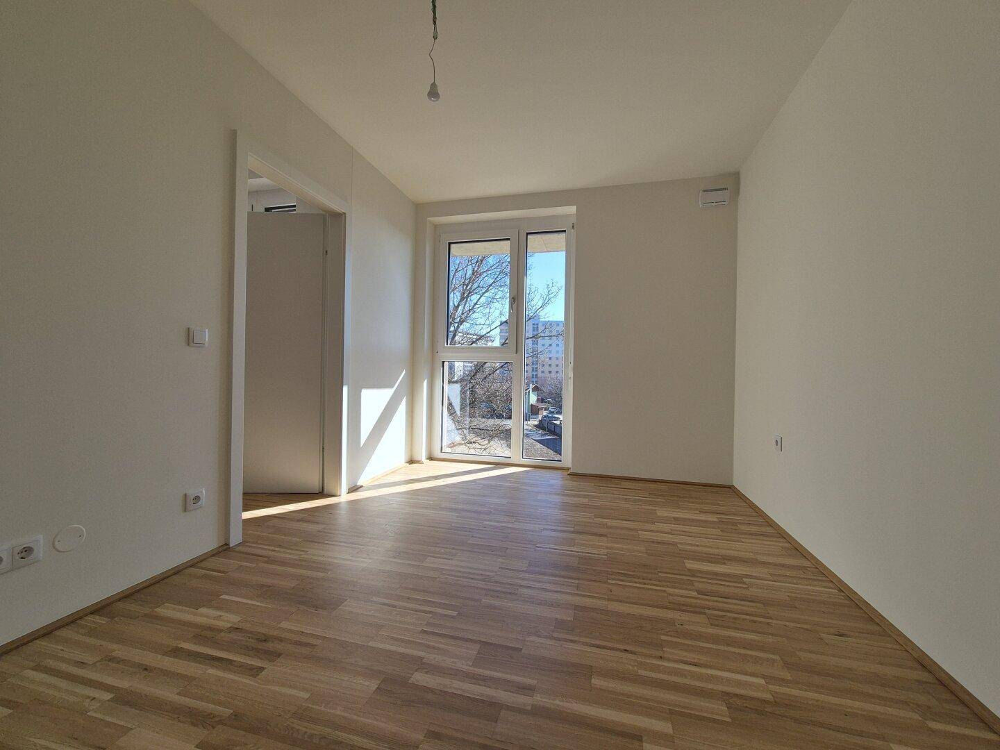 Lichtdurchfluteter Raum mit Holzparkett und großem Fenster, ideal als Schlafzimmer.