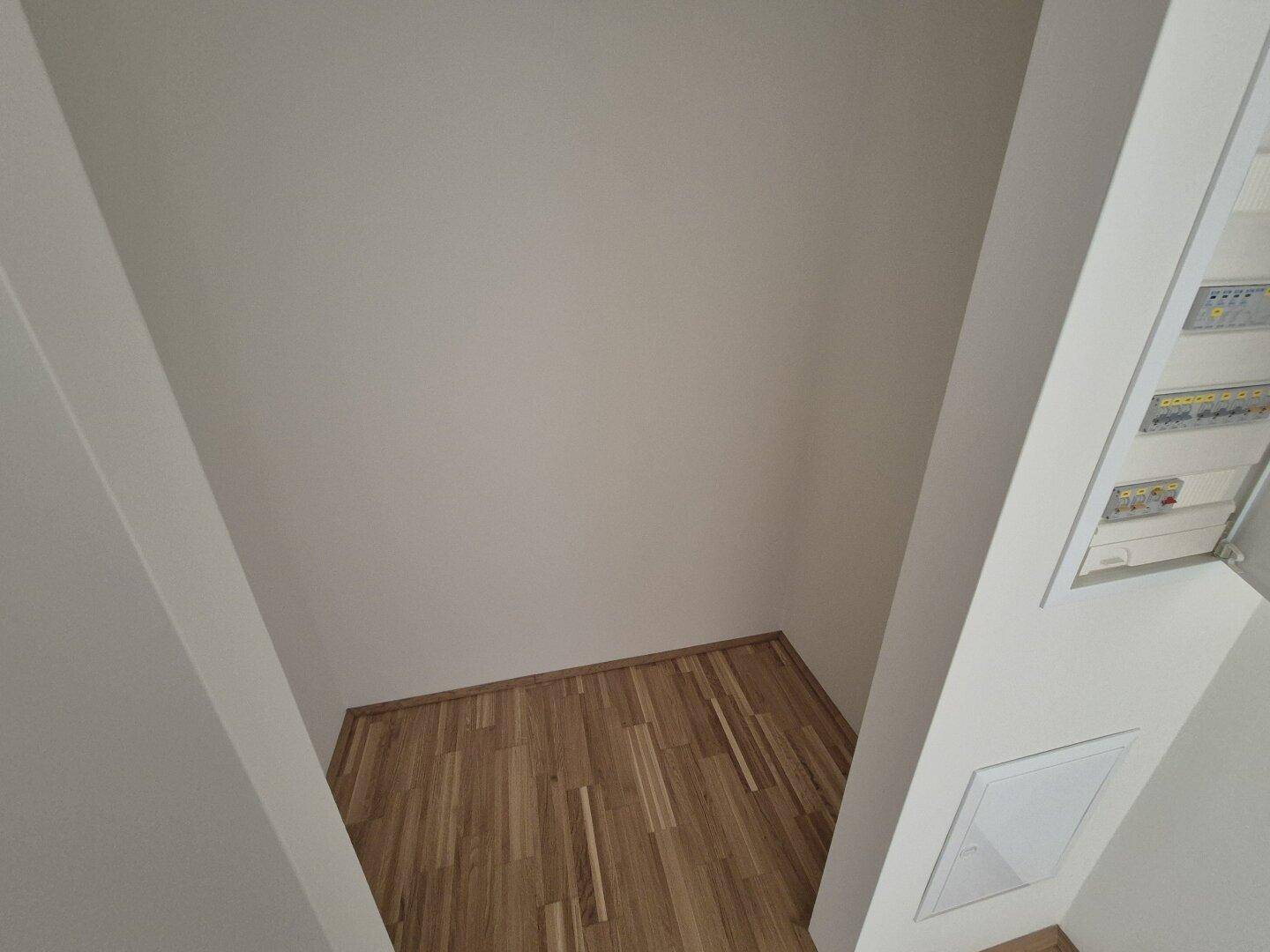 Kleiner, leerer Bereich mit Holzparkett und weiß gestrichenen Wänden.