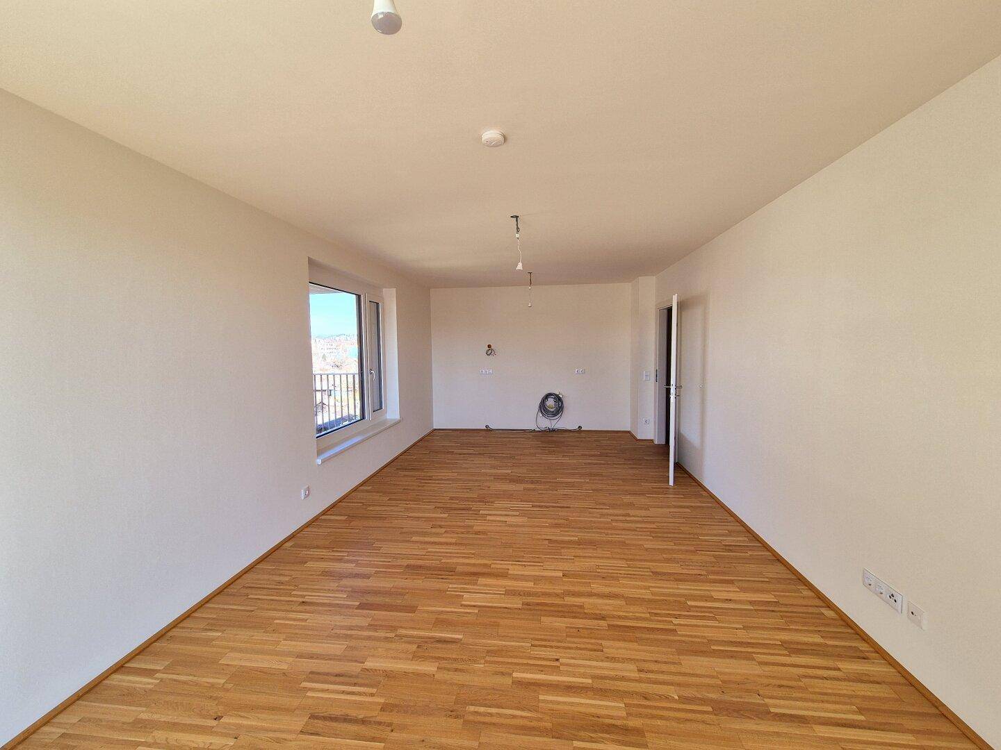 Geräumiges, unmöbliertes Zimmer mit Parkettboden und einem Fenster, das viel Tageslicht hereinlässt.