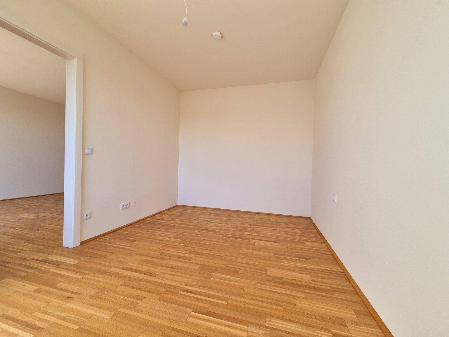 Leeres Zimmer mit hellem Parkettboden und weiß gestrichenen Wänden, bereit zur individuellen Gestaltung.