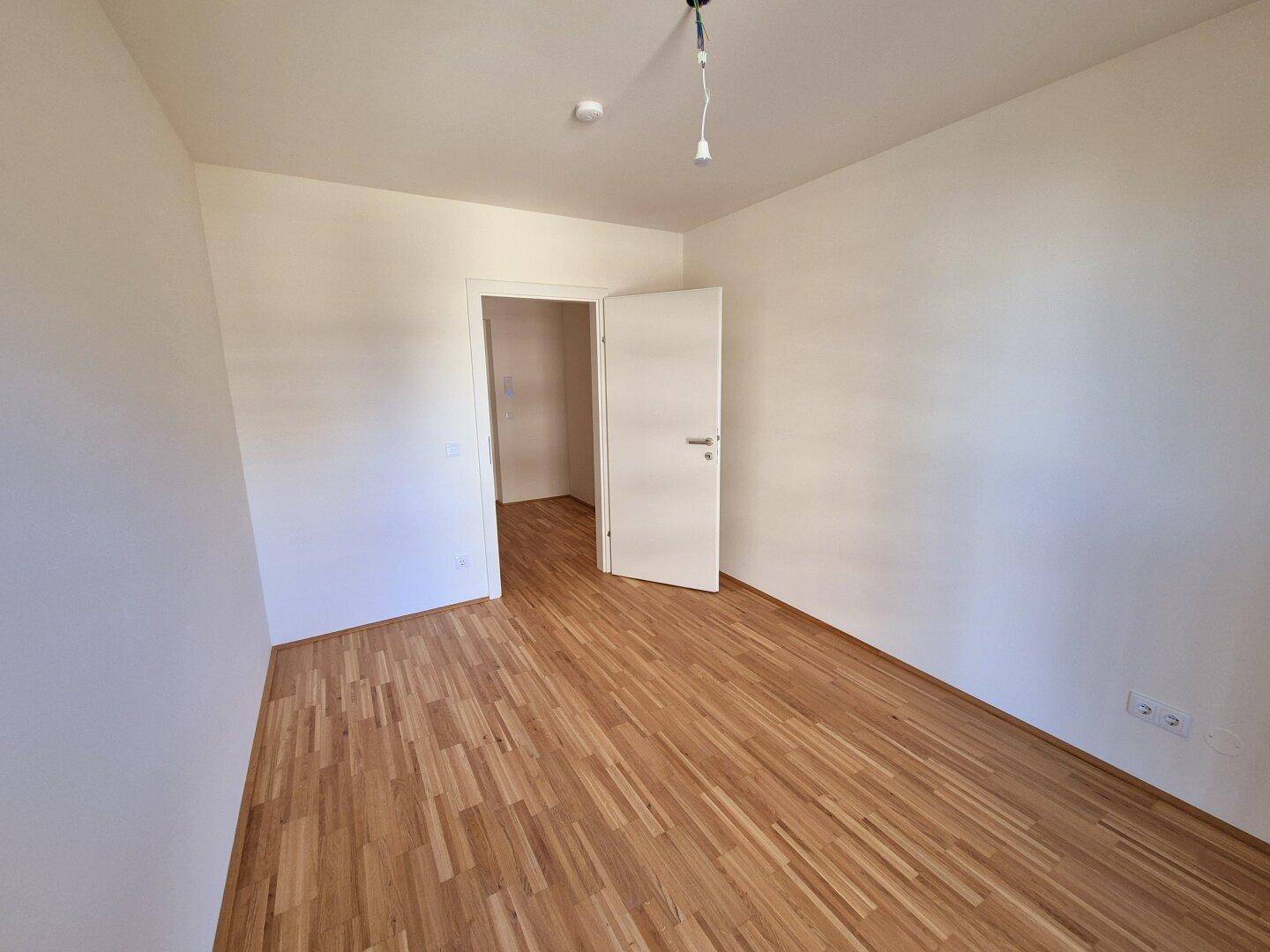 Unmöbliertes Zimmer mit Parkettboden und einer weißen Tür, ideal als Schlaf- oder Arbeitszimmer.