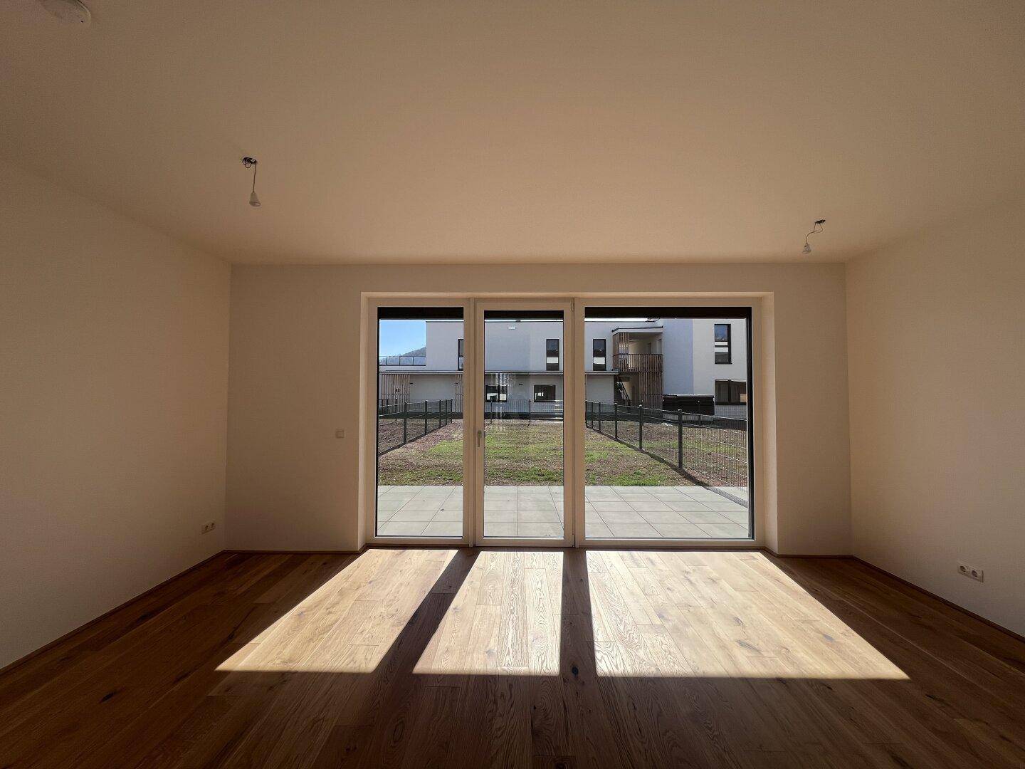 Helles, leeres Wohnzimmer mit Holzboden und großen Schiebetüren zur Terrasse.