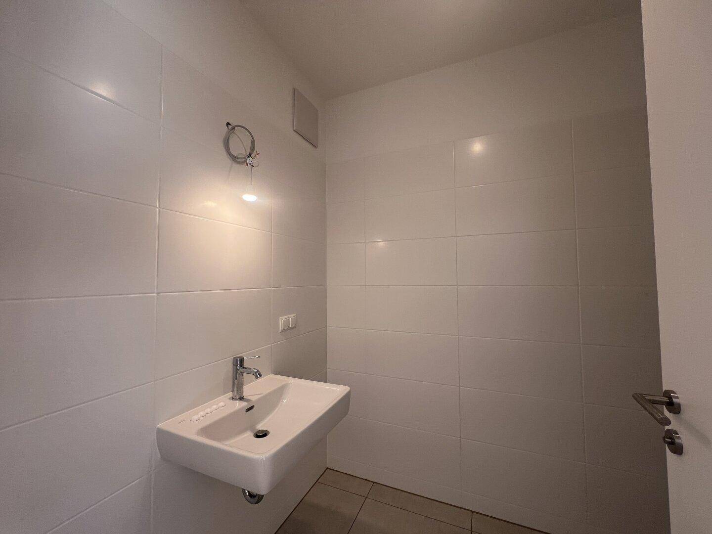 Modernes WC mit weiß gefliesten Wänden und einem einzelnen Waschbecken.