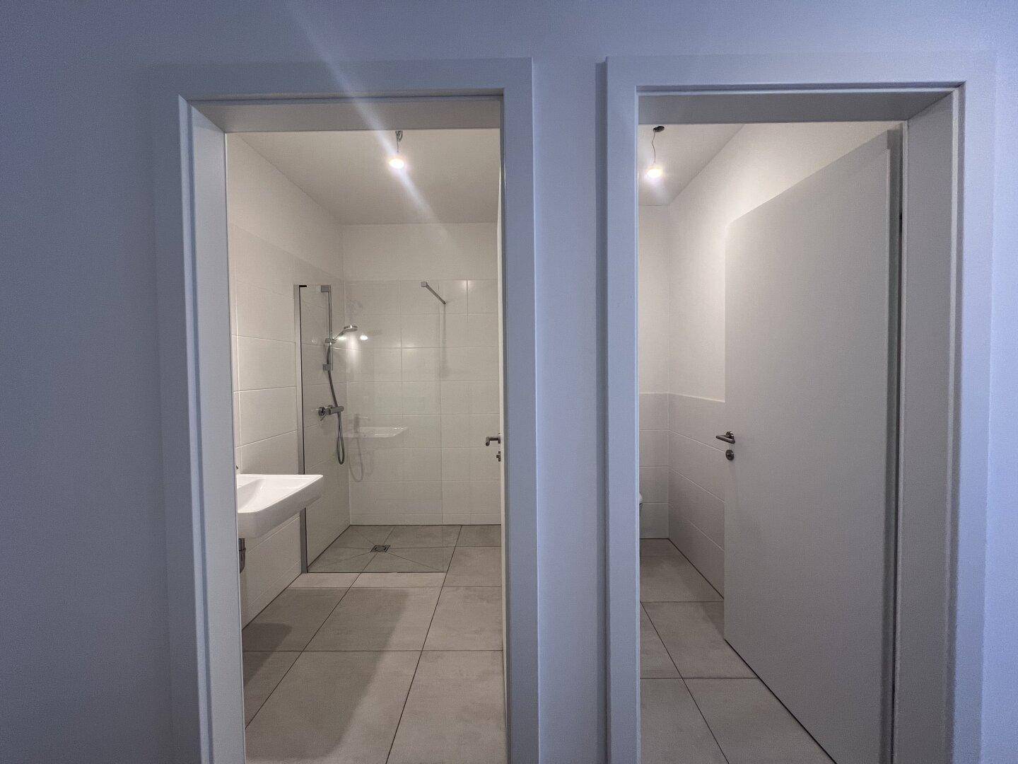 Blick vom Flur in ein modernes Badezimmer mit Dusche und eine separate Gästetoilette.