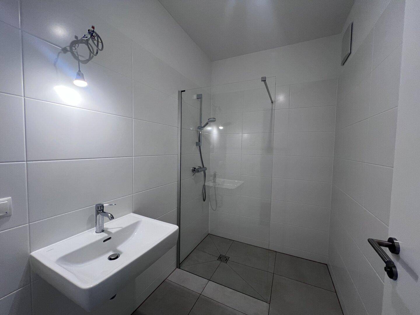 Modernes Badezimmer mit weiß gefliesten Wänden, ebenerdiger Dusche und Einzelwaschbecken.