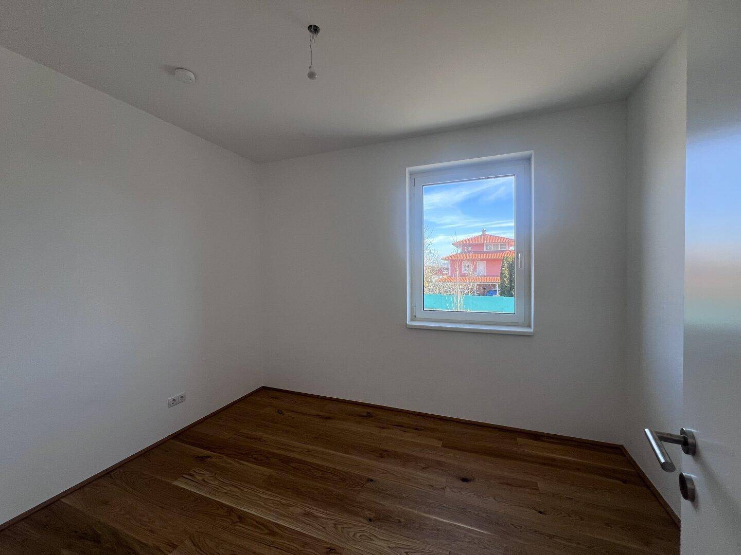 Helles Schlafzimmer mit neuem Holzfußboden und einem Fenster, das einen Blick ins Grüne bietet.