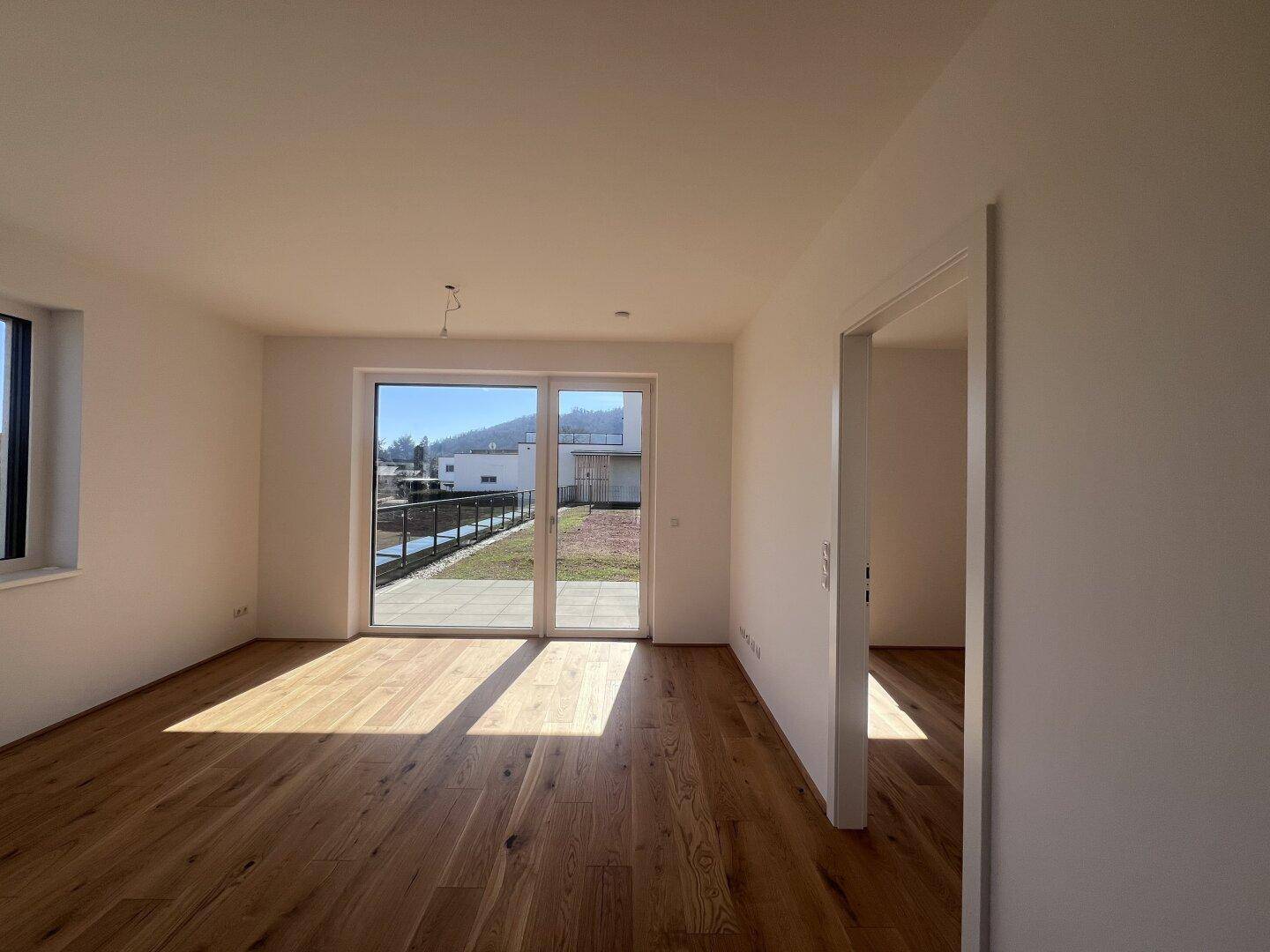 Lichtdurchfluteter Wohnbereich mit elegantem Holzparkett und breiter Glastür, die auf eine Außenterrasse führt.