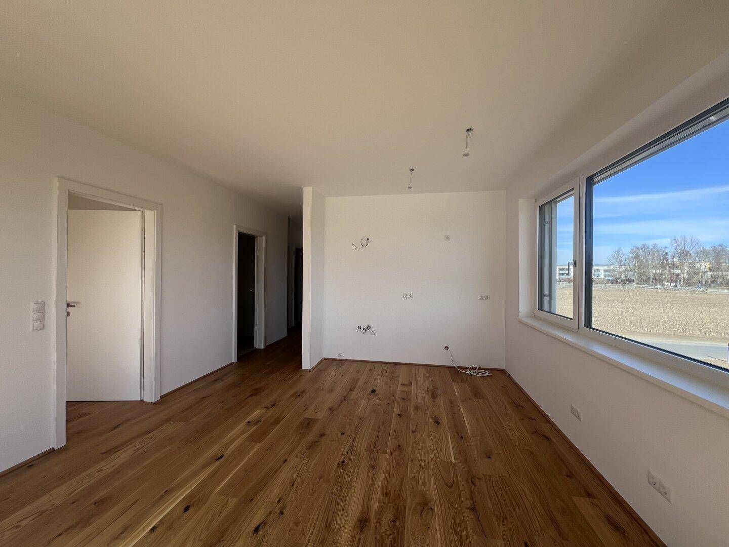 Offener Wohnbereich mit elegantem Holzfußboden und großen Fenstern, die den Raum mit Licht füllen.