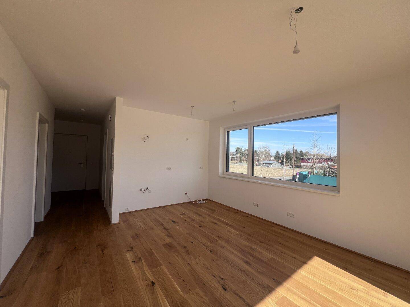 Geräumiger Wohnbereich mit hochwertigem Holzfußboden und großen Fenstern, die eine weite Aussicht ermöglichen.