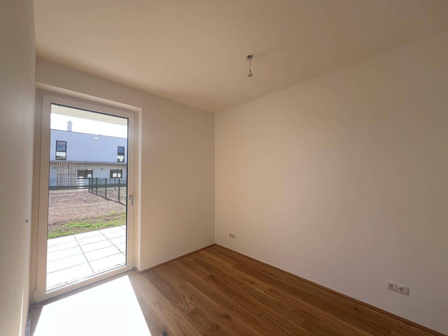 Helles Schlafzimmer mit Holzfußboden und direktem Zugang zu einem kleinen Außenbereich, ideal für frische Luft.