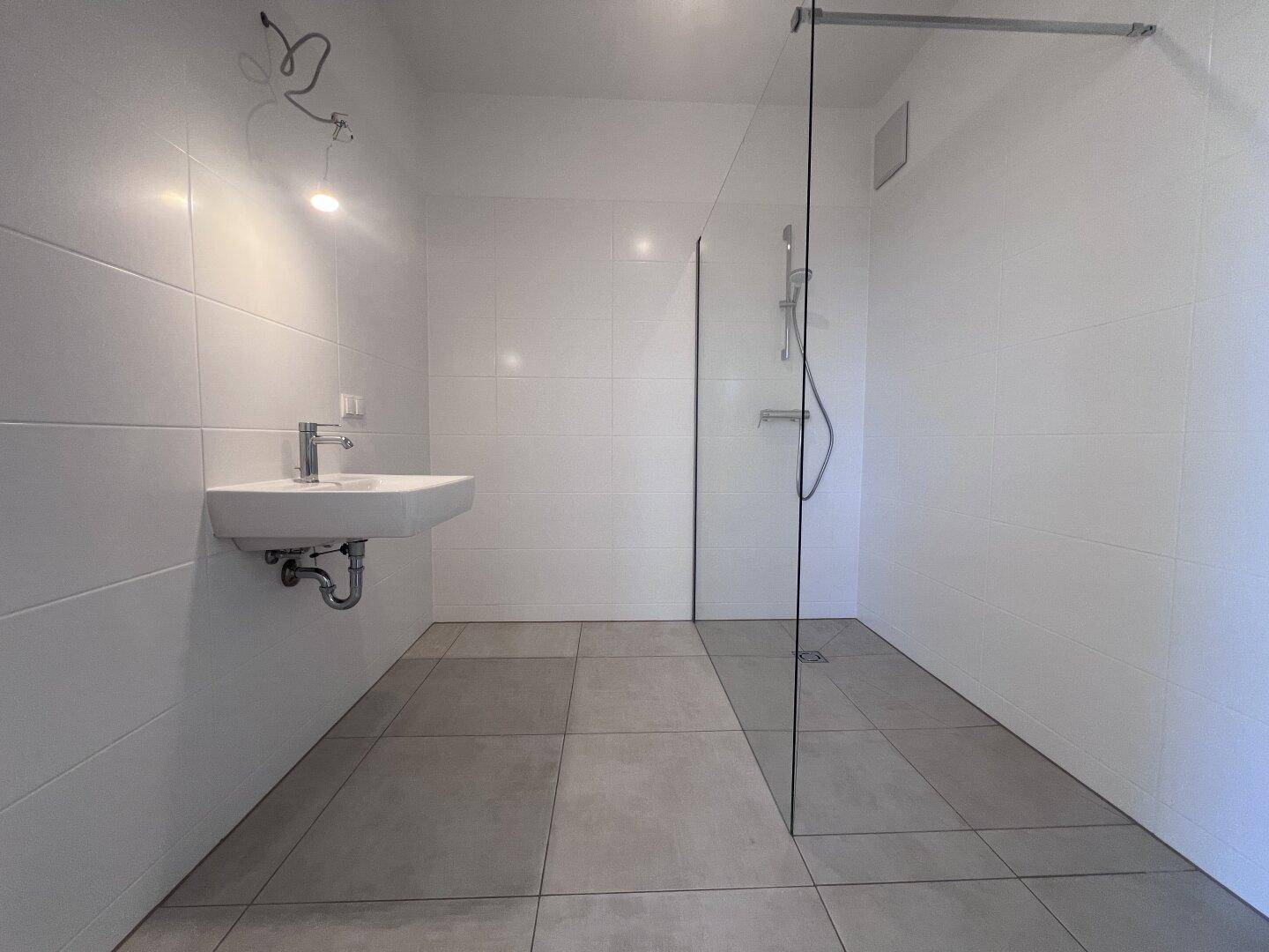 Modernes Badezimmer mit weißen Wandfliesen, grauen Bodenfliesen und einer geräumigen begehbaren Dusche.