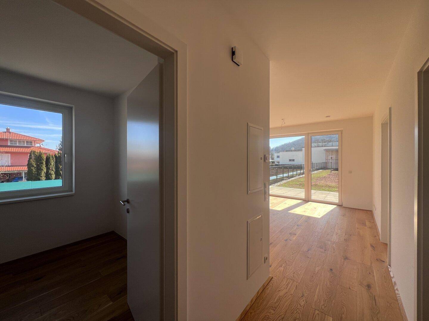 Heller Flur mit Holzfußboden, der zu weiteren Räumen führt und einen Blick in einen sonnigen Raum bietet.