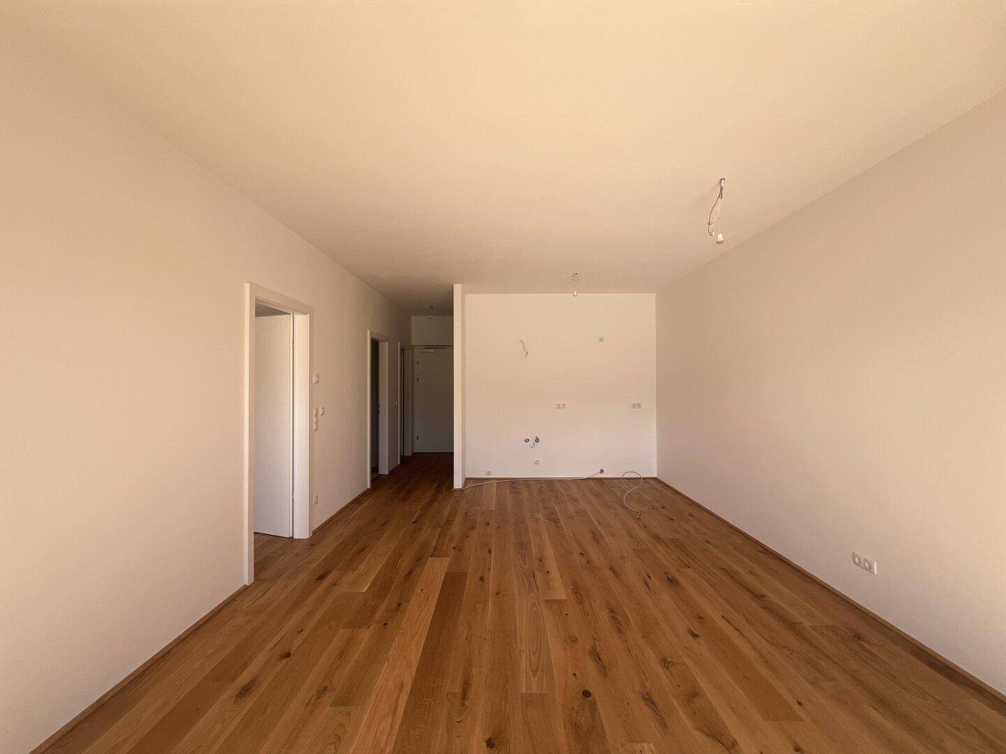 Geräumiger, heller Wohnbereich mit neuem Holzparkett und weißen Wänden, bereit für die Einrichtung.