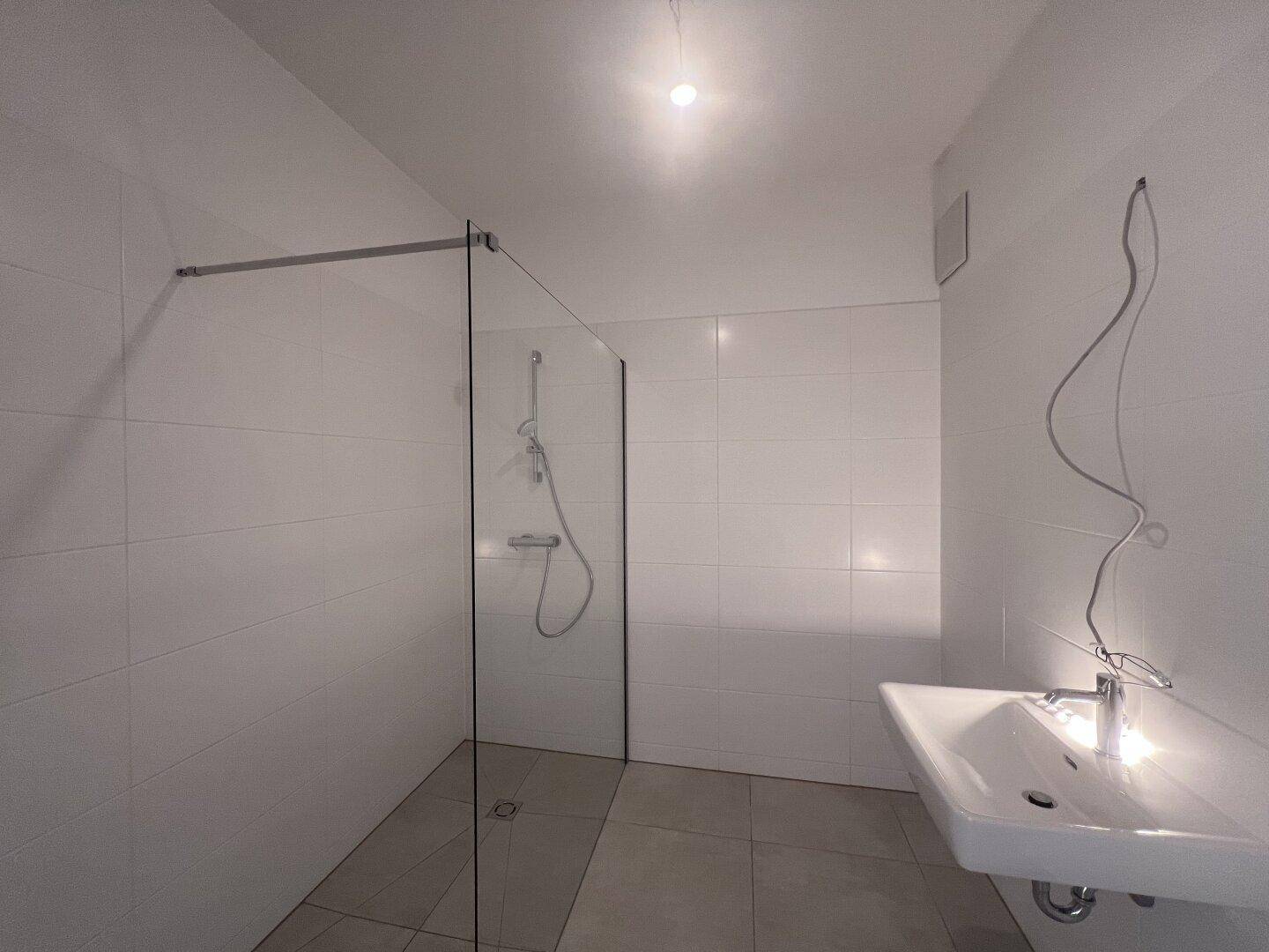 Modernes Badezimmer mit weiß gefliesten Wänden, begehbarer Dusche und wandmontiertem Waschbecken.