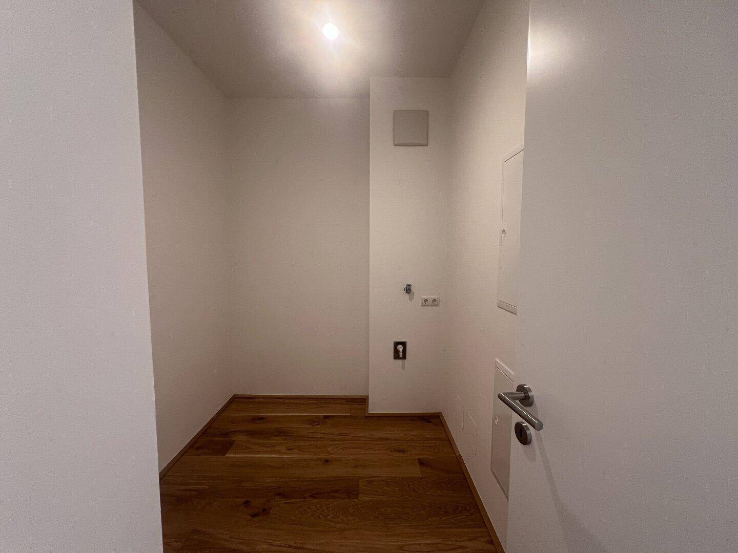 Kleiner Hauswirtschaftsraum mit Holzfußboden und Anschlüssen für Waschmaschine oder Lagerung.