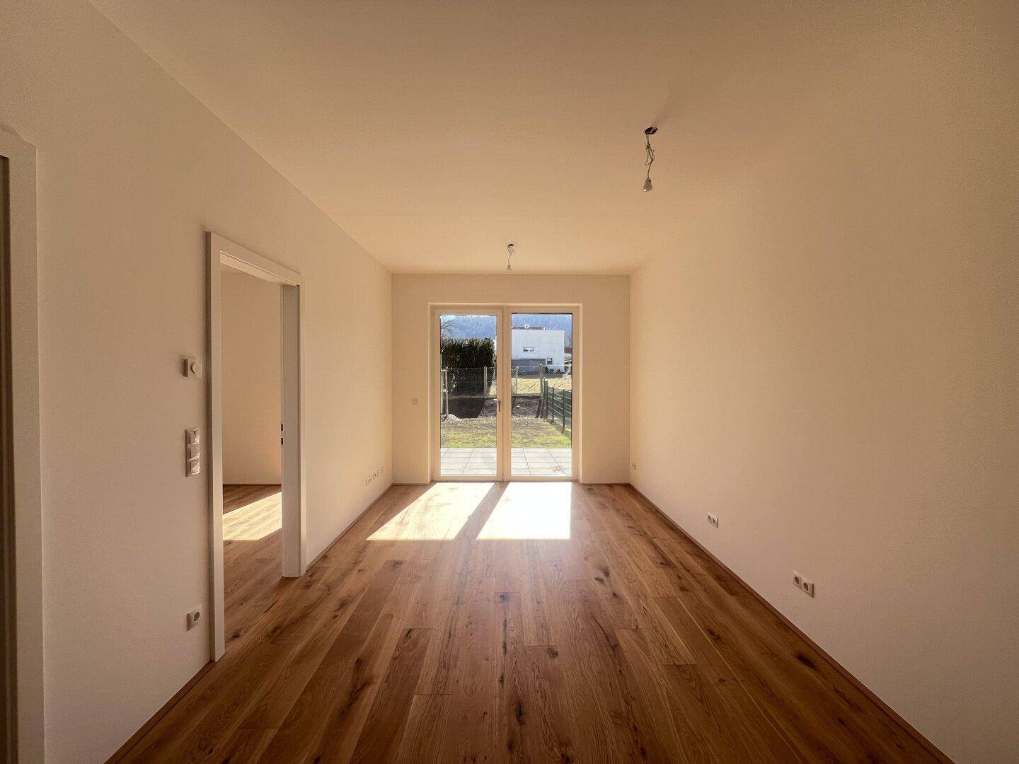 Heller, leerer Raum mit Holzboden und Zugang zu einem kleinen Gartenbereich.