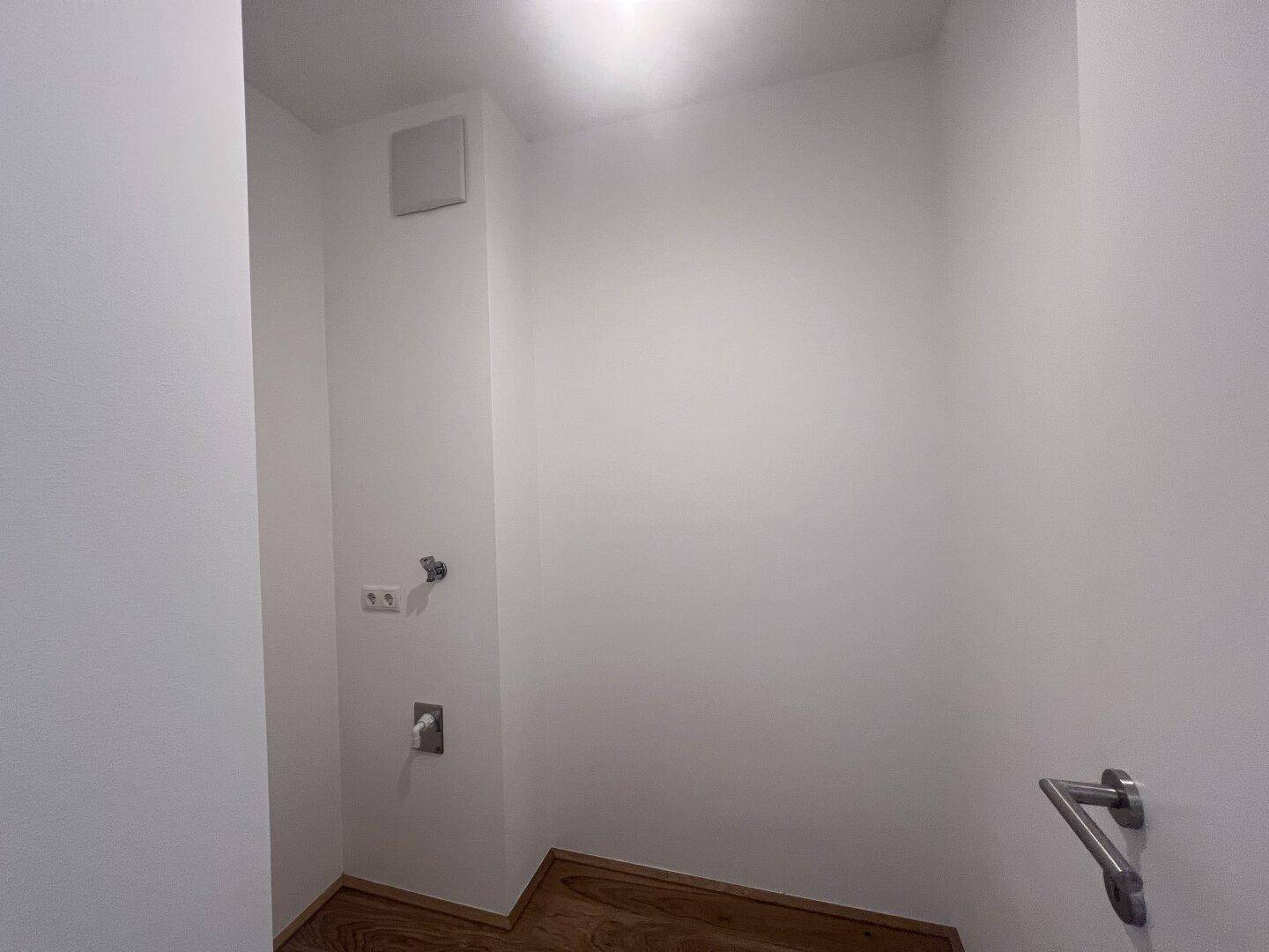 Kleiner Hauswirtschaftsraum mit Holzboden und Anschlüssen für Waschmaschine oder Trockner.