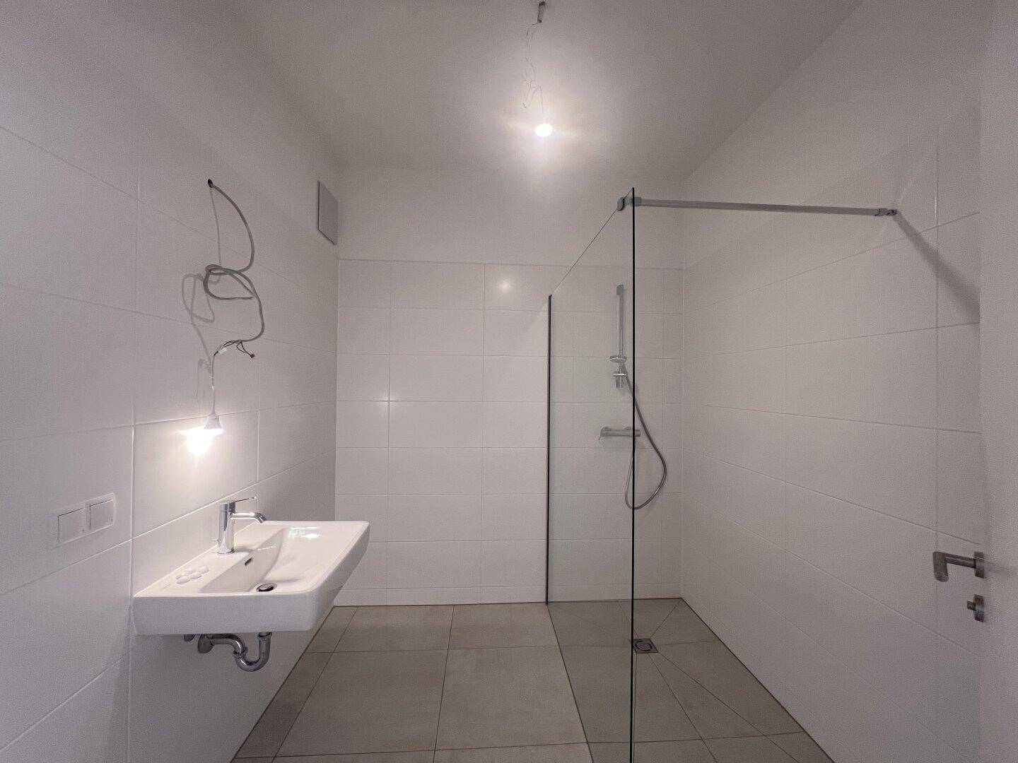 Modernes Badezimmer mit weißen Fliesen, wandhängendem Waschbecken und begehbarer Dusche.