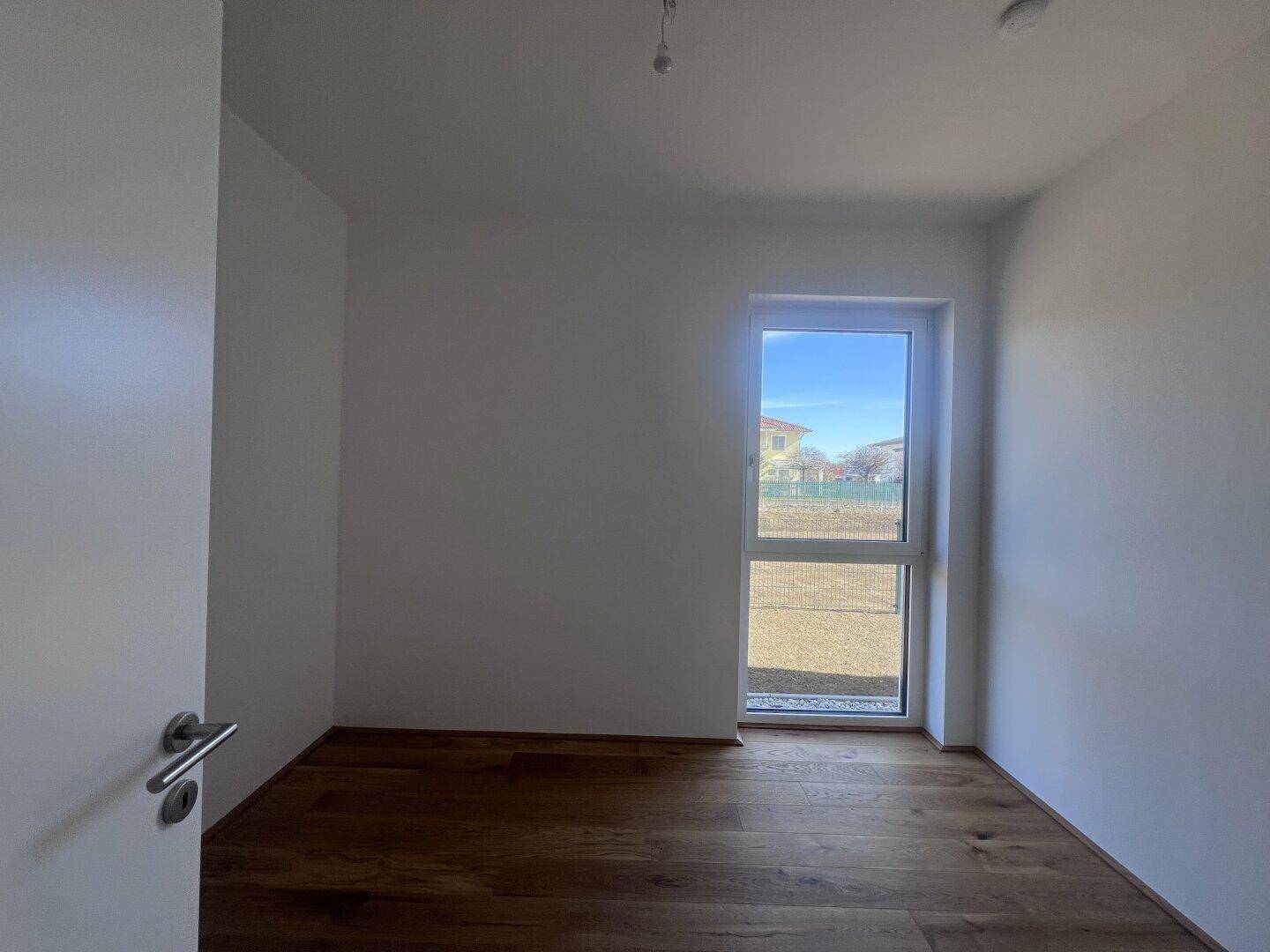 Helles Schlafzimmer mit Holzboden und einem großen Fenster, das viel Tageslicht hereinlässt.