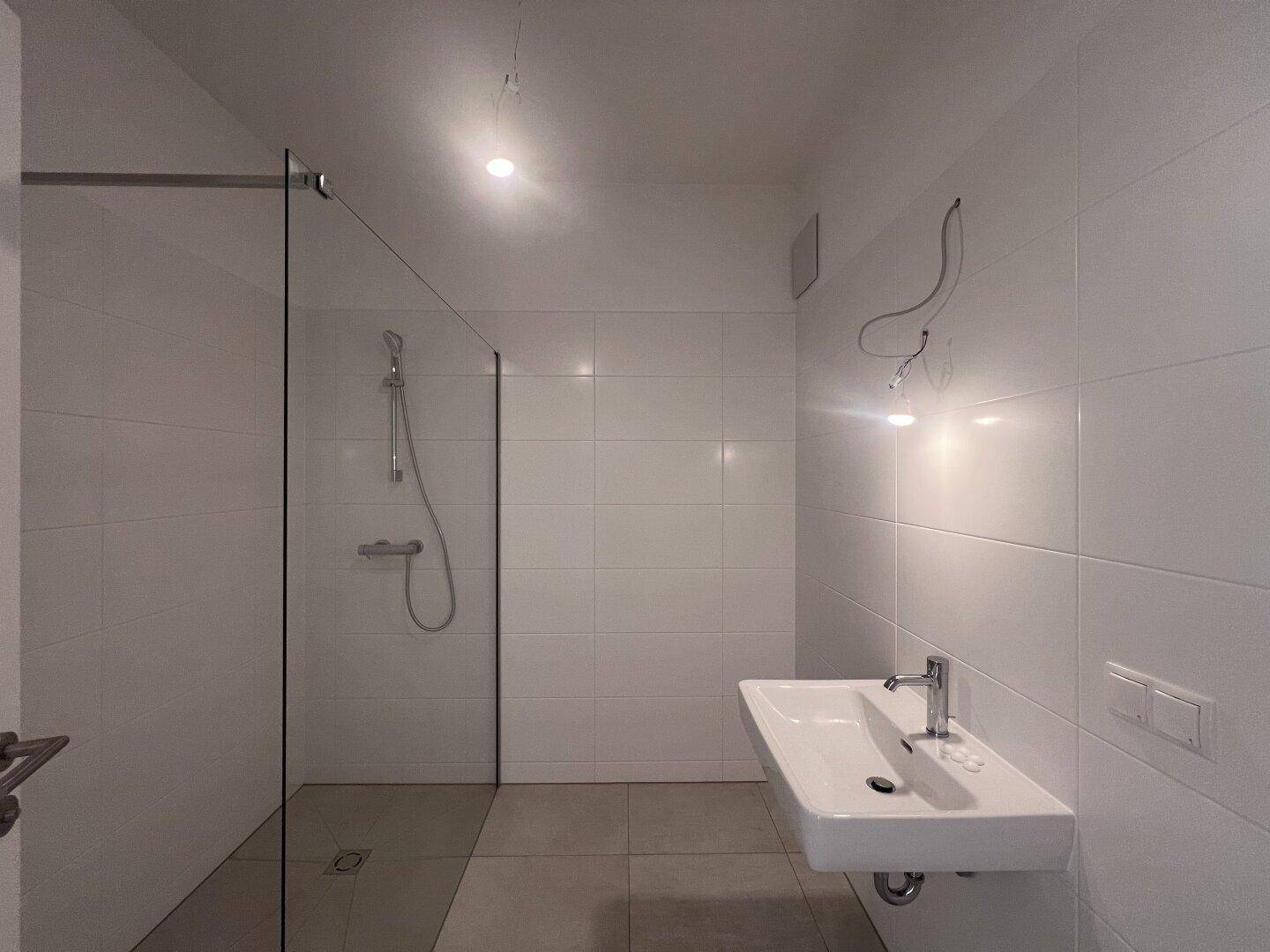 Modernes Badezimmer mit weiß gefliesten Wänden, ebenerdiger Dusche und schwebendem Waschbecken.