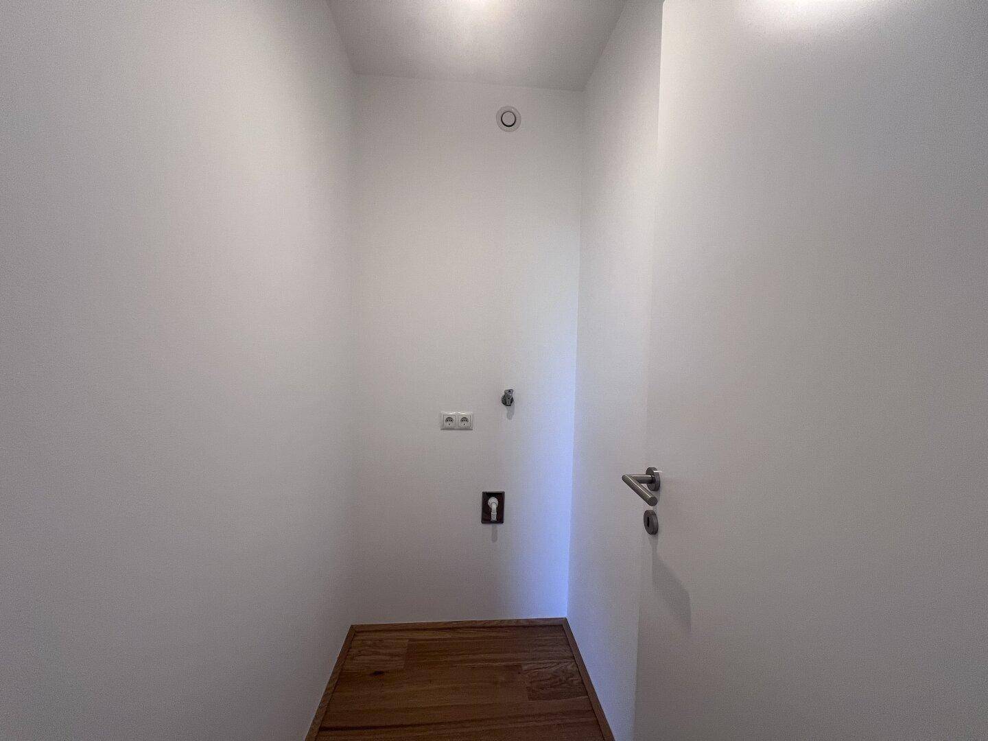 Praktischer Hauswirtschaftsraum mit Holzboden und Anschlüssen für Waschmaschine und Trockner.