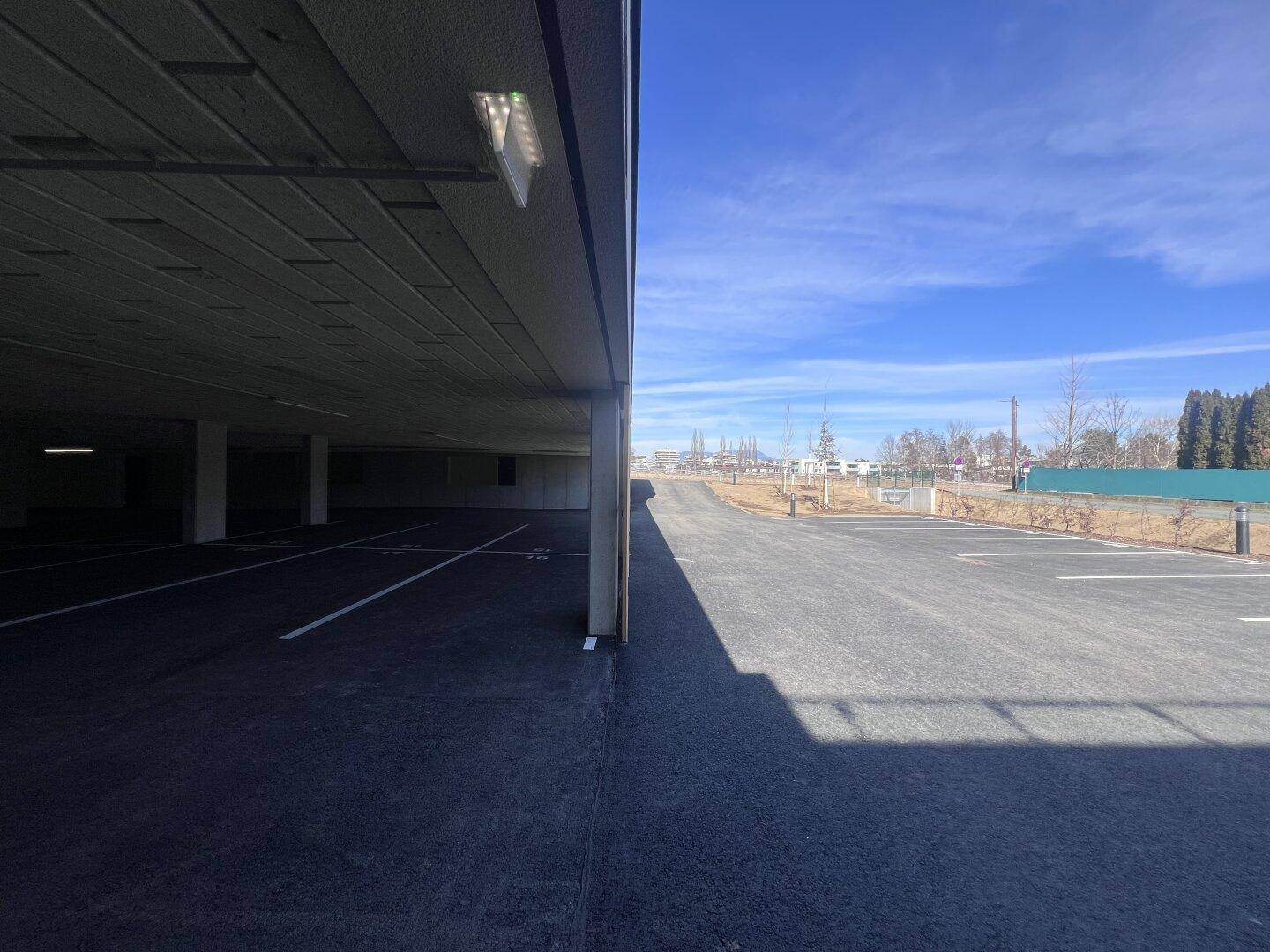 Außenparkplätze und Zufahrt zu einer Tiefgarage unter blauem Himmel.