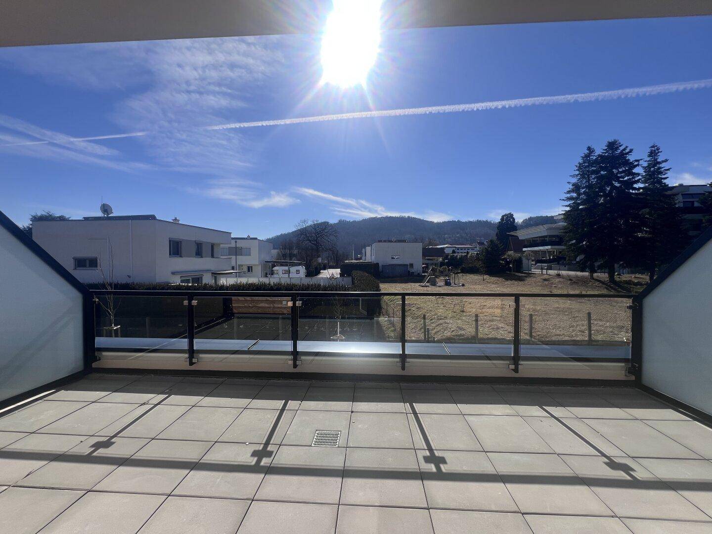 Sonniger Terrassenbereich mit Glasgeländer und weitem Blick auf die grüne Umgebung.