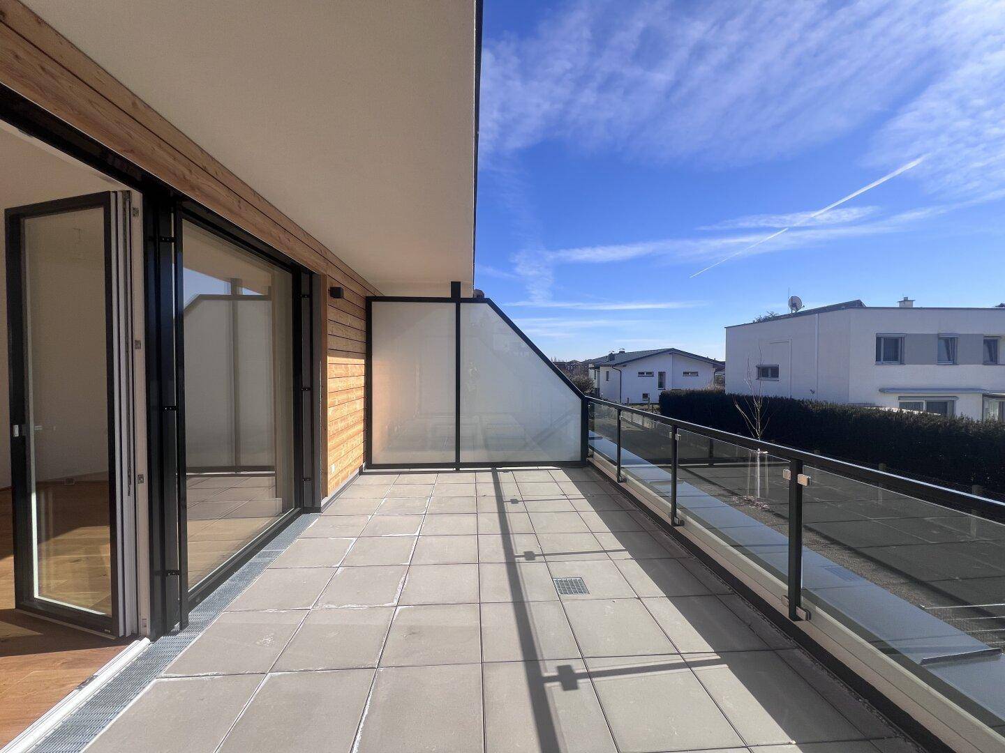 Moderne Terrasse mit Holzverkleidung und Glasgeländer, bietet viel Platz im Freien.