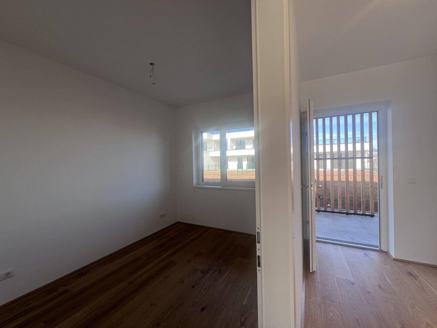 Helles Zimmer mit Parkettboden und Fenster, bietet Zugang zu einem Außenbereich.