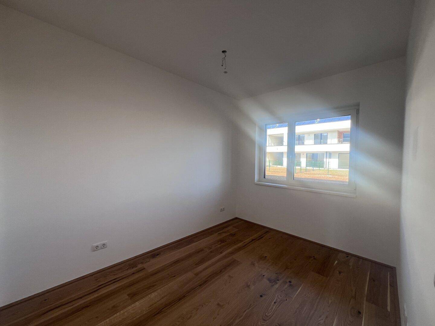 Freundliches Zimmer mit Parkettboden und großem Fenster, ideal als Schlaf- oder Arbeitszimmer.