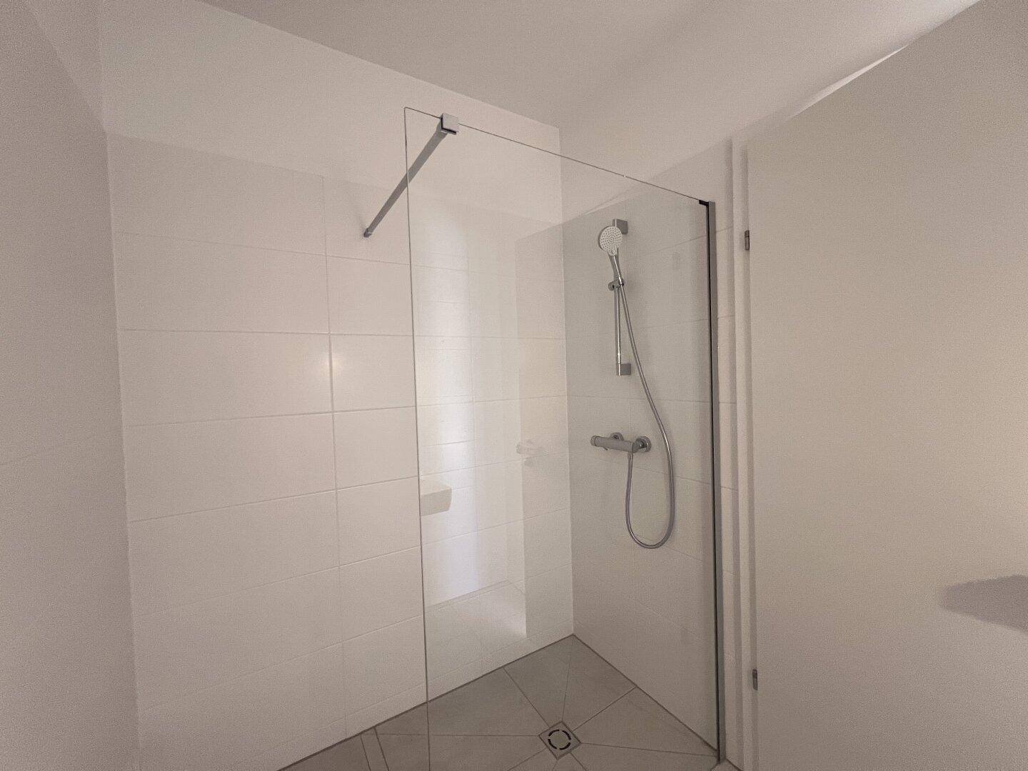 Helles Badezimmer mit begehbarer Dusche und modernen weißen Fliesen.