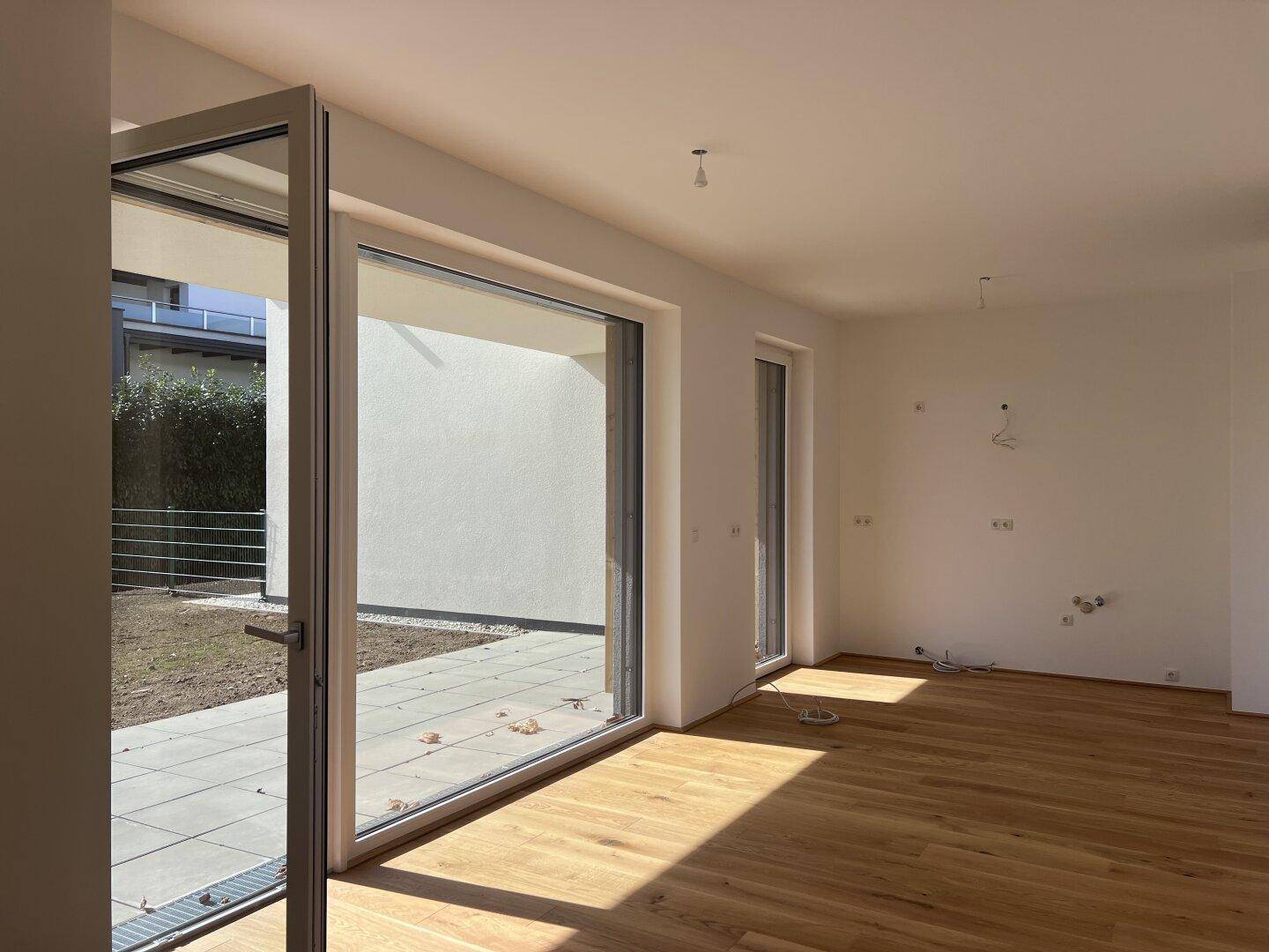 Heller, leerer Wohnraum mit Holzboden und Zugang zu einer Terrasse oder Garten.