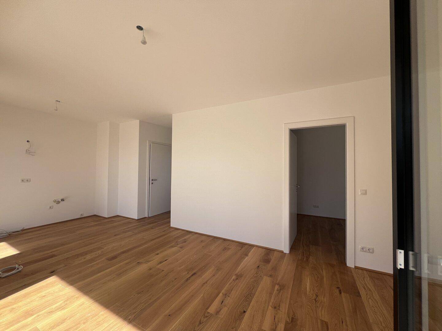 Geräumiger, heller Wohnbereich mit Holzboden und weiß gestrichenen Wänden.
