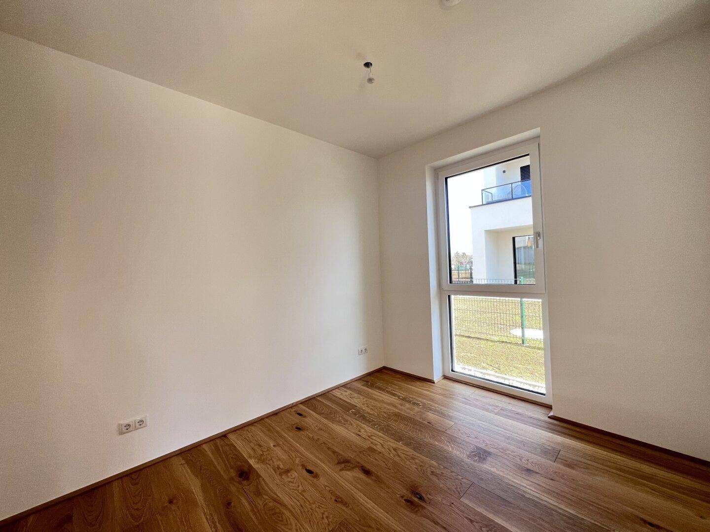 Helles Schlafzimmer mit Holzboden und großem Fenster mit Blick ins Grüne.