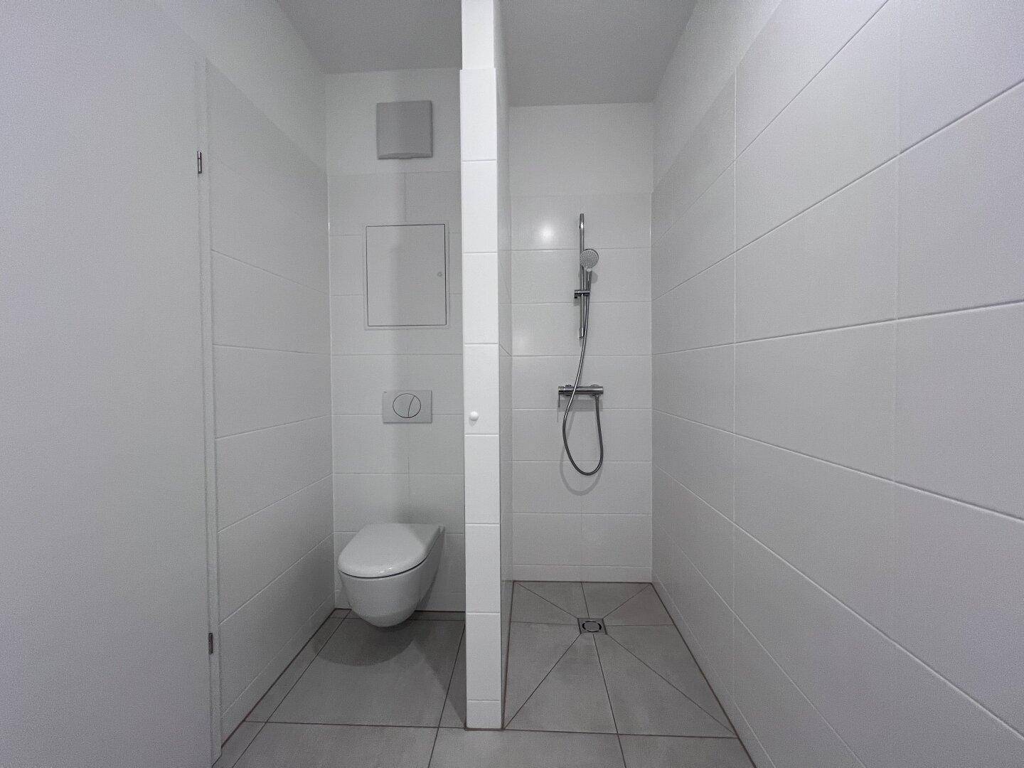 Modernes Badezimmer mit weißen Fliesen, wandhängendem WC und begehbarer Dusche.