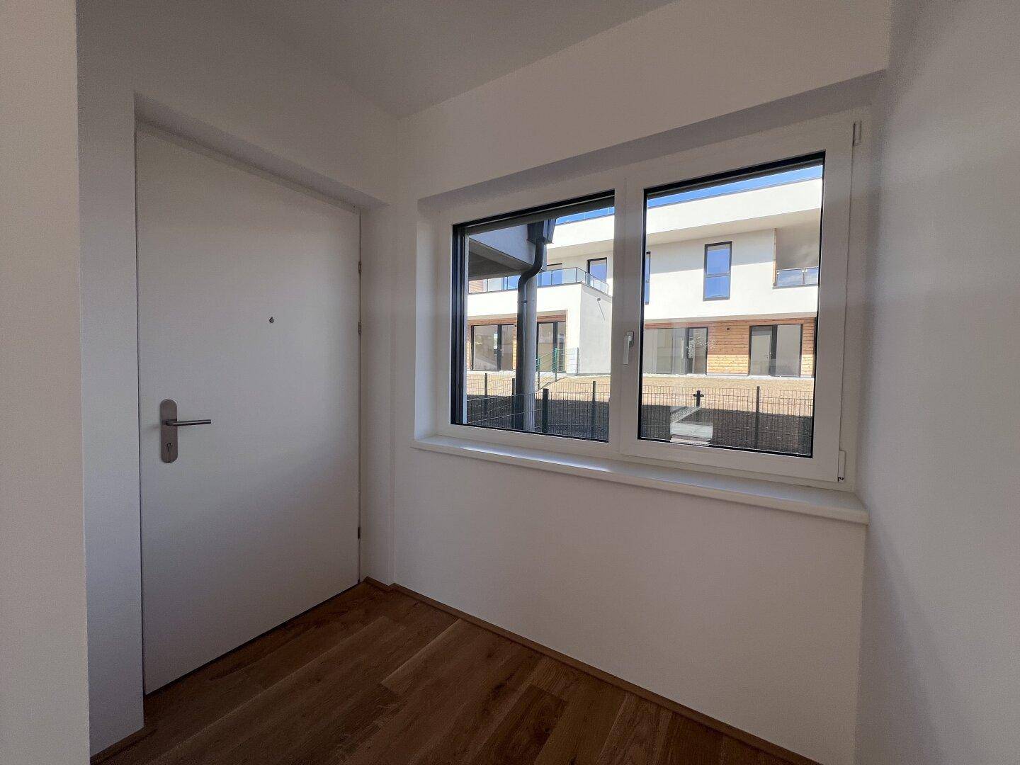Heller Eingangsbereich mit Holzboden, weißer Tür und Fenster mit Blick auf die Nachbargebäude.