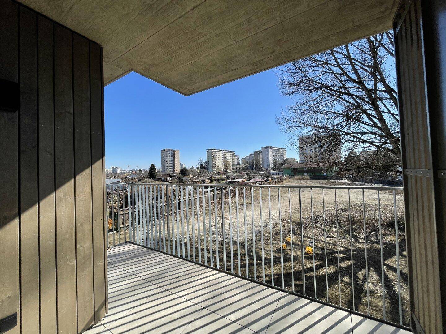 Sonniger Balkon mit Fliesenboden und weitem Blick auf die städtische Umgebung und Bäume.