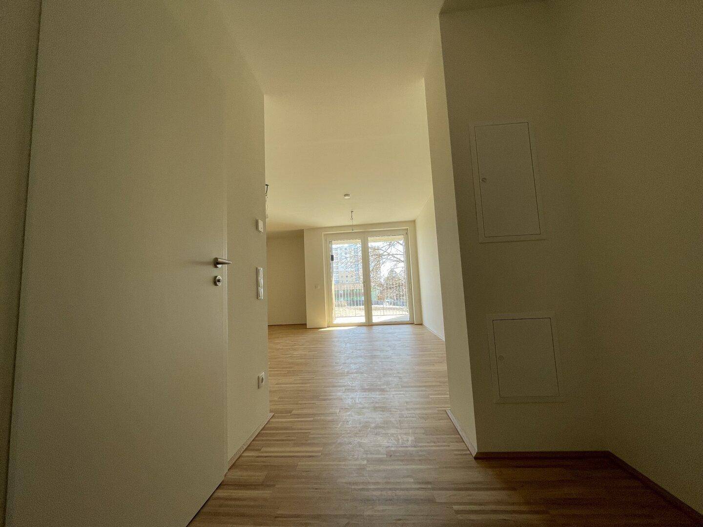 Heller Eingangsbereich mit Parkettboden, der in einen lichtdurchfluteten Wohnraum führt.