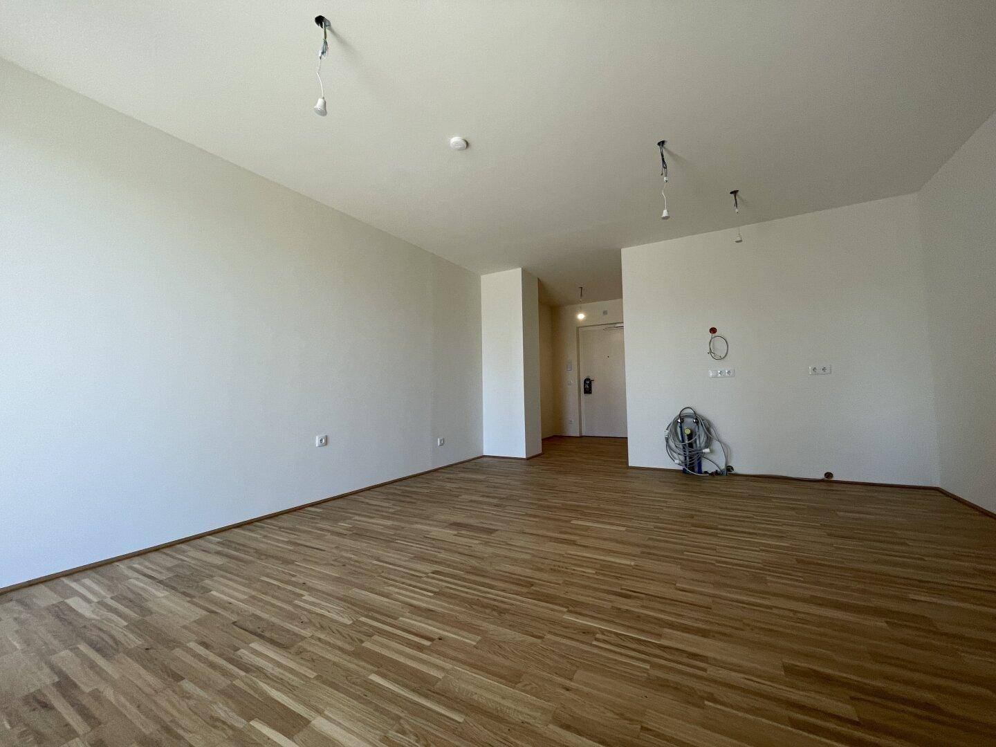 Geräumiger, leerer Wohnraum mit hellem Parkettboden und weißen Wänden, bereit zum Einzug.