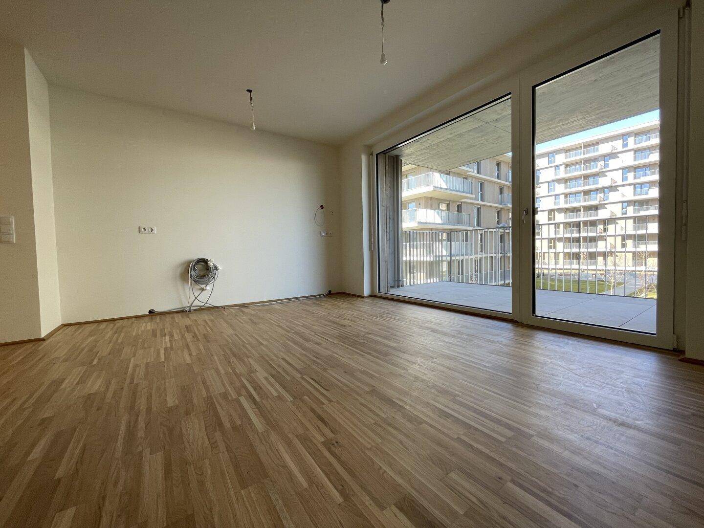 Lichtdurchfluteter Wohnbereich mit Zugang zum Balkon und Blick auf die umliegenden Neubauten.