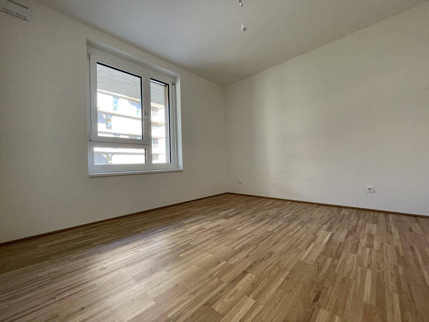 Helles Schlafzimmer mit Parkettboden und großem Fenster, ideal für eine ruhige Atmosphäre.