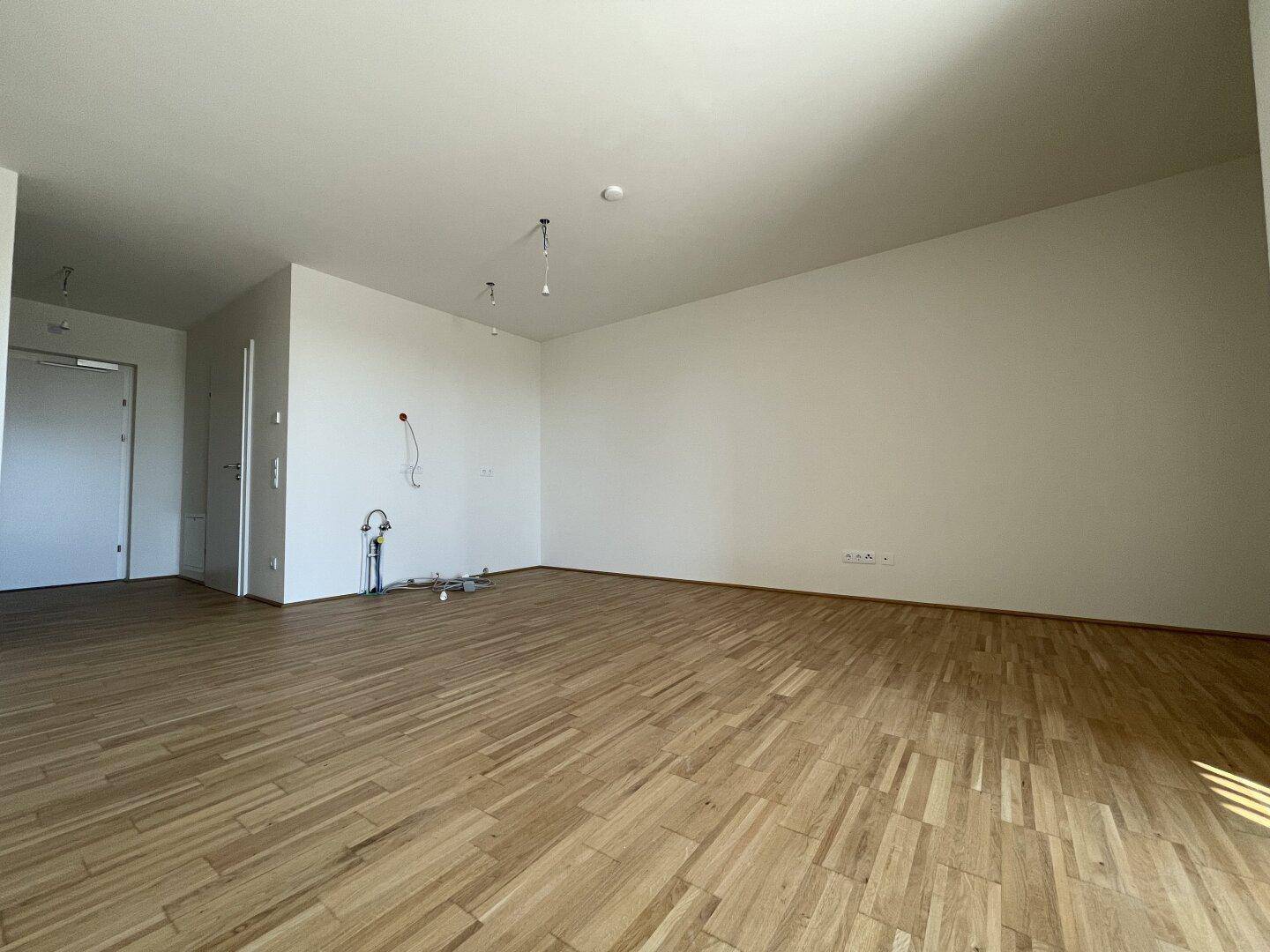 Heller Wohnbereich mit Parkettboden und weißen Wänden, bereit für die Einrichtung.