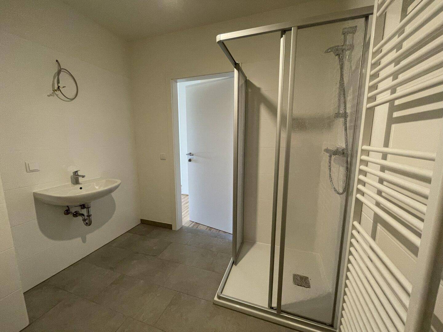 Modernes Badezimmer mit Duschkabine, Waschbecken und beheiztem Handtuchhalter.