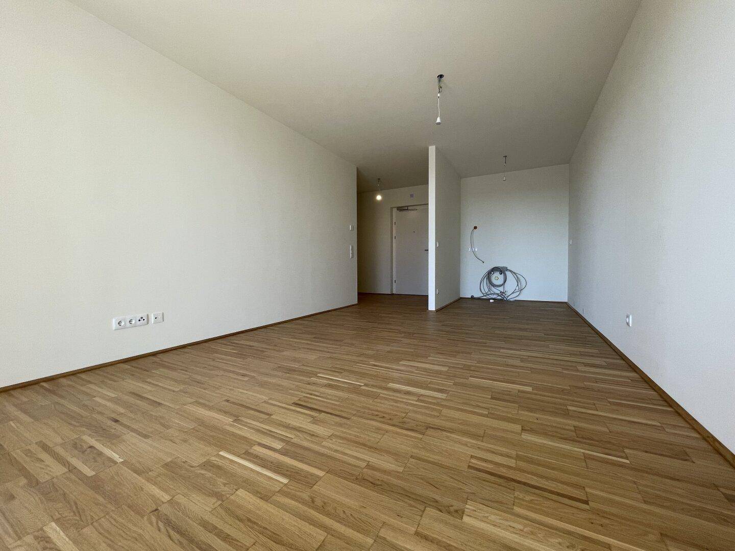 Geräumiger, heller Raum mit Eichenparkett und weiß gestrichenen Wänden, bereit zum Einzug.