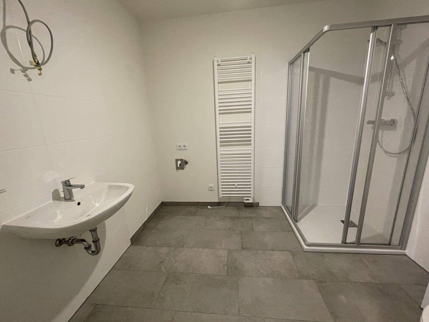 Modernes Badezimmer mit Duschkabine, Waschbecken und beheiztem Handtuchhalter.