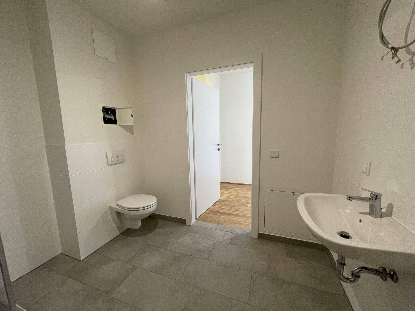 Funktionales Badezimmer mit wandhängendem WC, Waschbecken und modernen Fliesen.